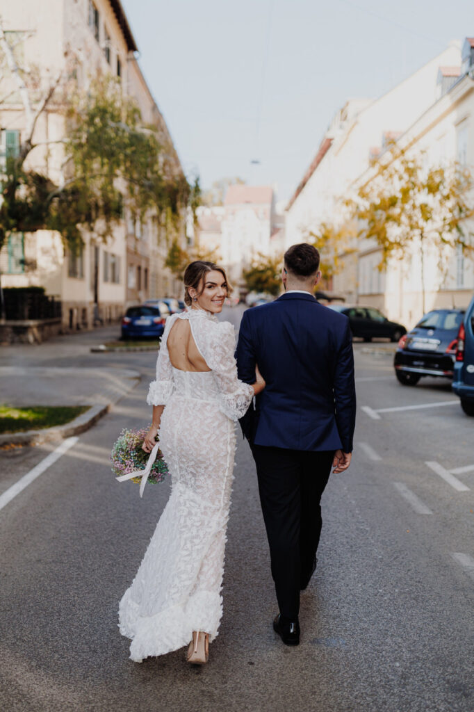 Newlyweds taking a walk and holding hands in streets of Zagreb. Bride wearing EnvyRoom dress.